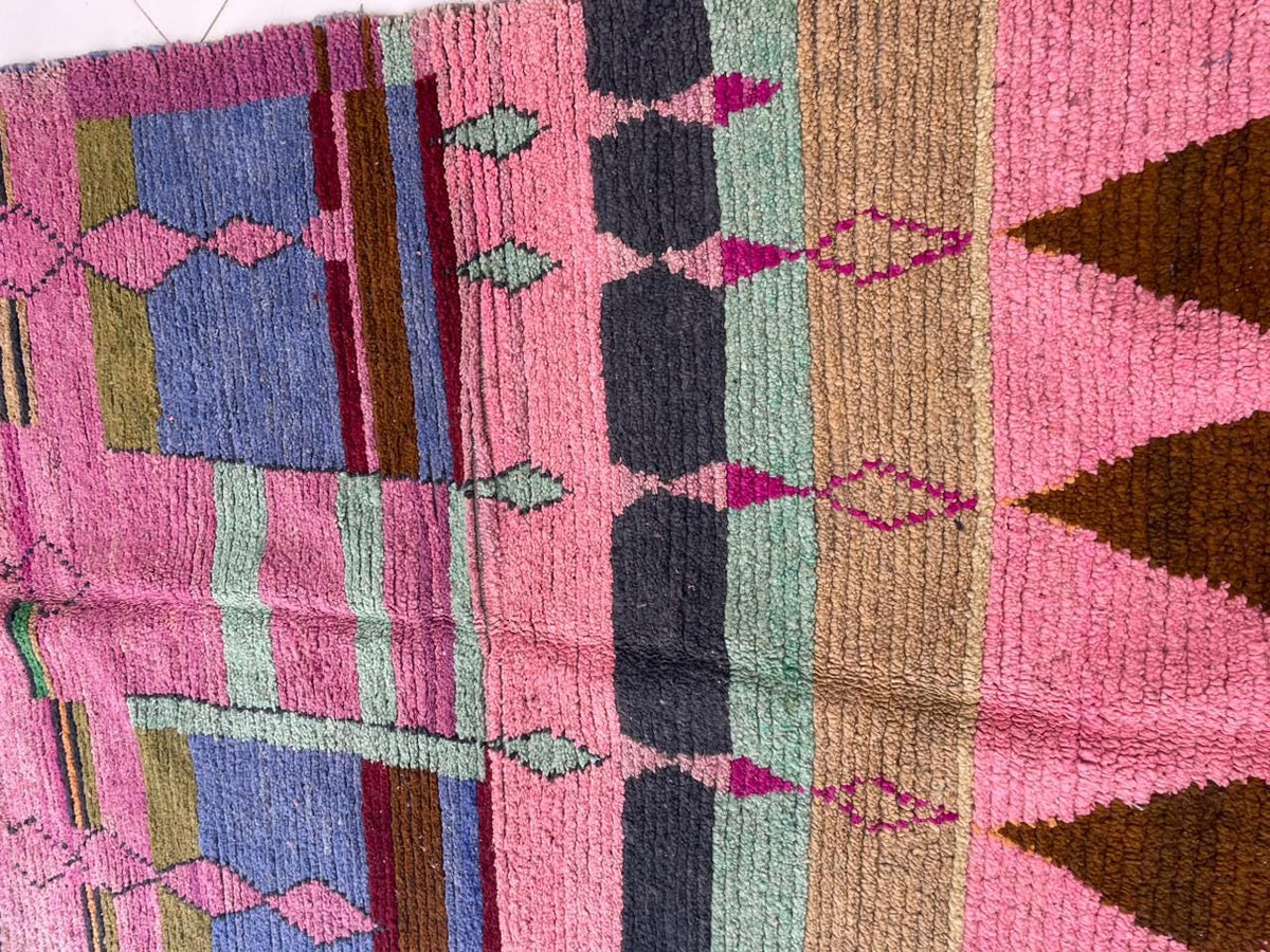 Top view of a pink vintage Moroccan rug featuring geometric patterns and fringe edges.