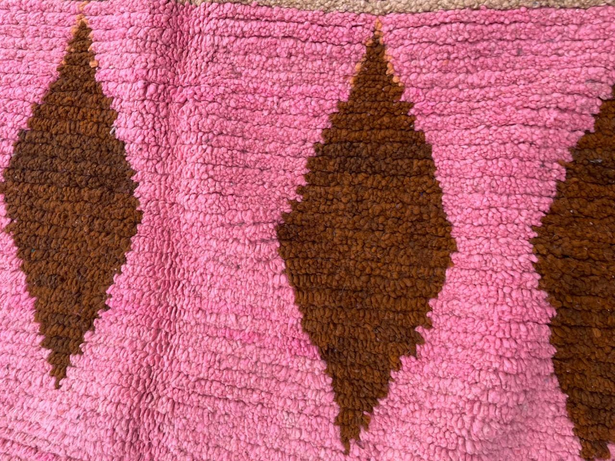 Detail view of a pink Moroccan rug displaying a diamond pattern and textured surface.