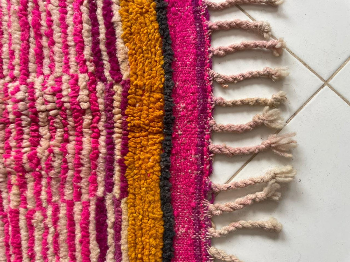 Close-up detail of a pink Moroccan rug with fringe edges and a striped pattern.
