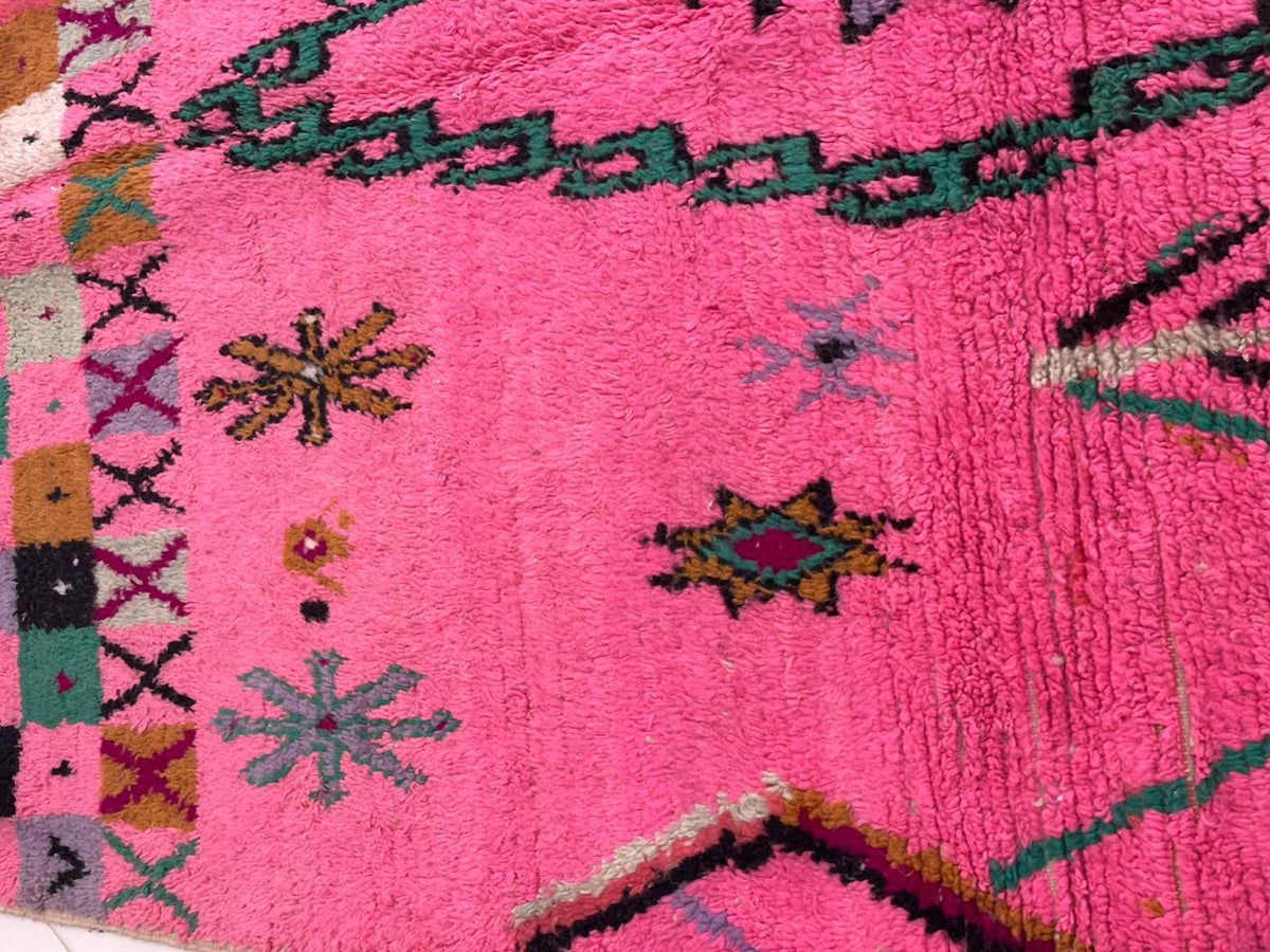 Detail close-up of a pink Moroccan rug with floral designs and textured wool.