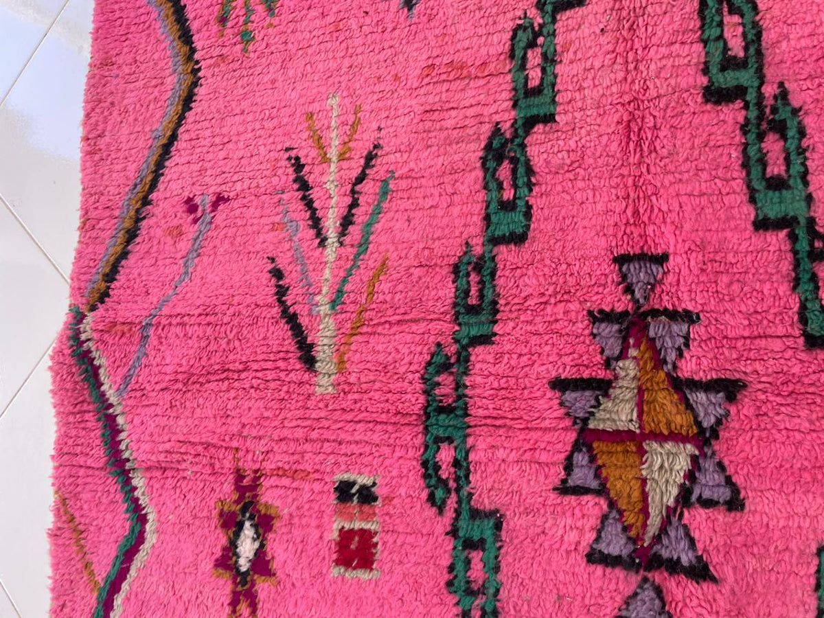 Detail close-up of a pink Moroccan rug with intricate designs and fringe edges.