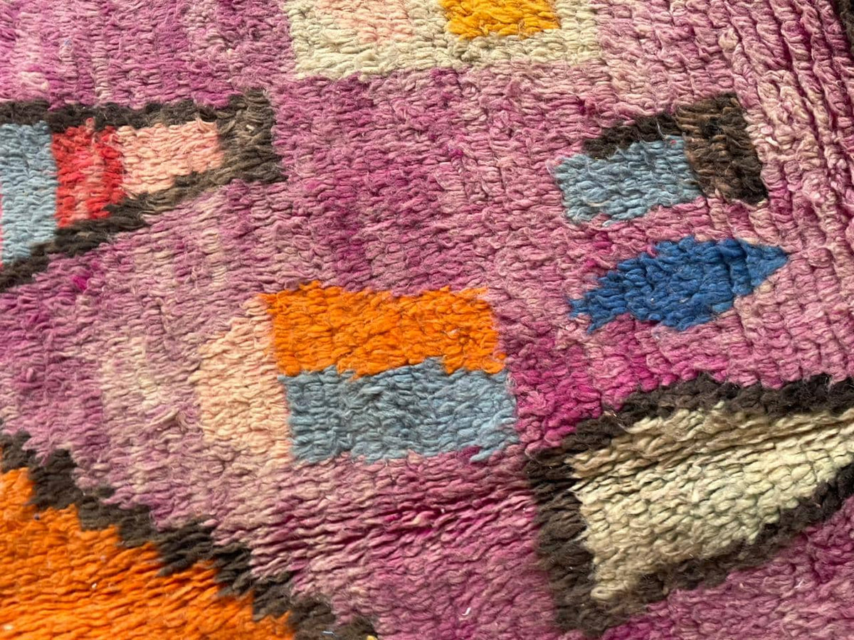 Close-up detail of geometric shapes on a vintage Moroccan rug in orange, purple, and red.