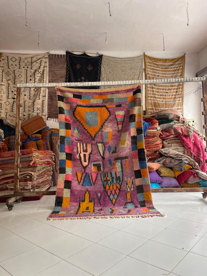 Lifestyle shot of a vintage Moroccan rug featuring geometric patterns in purple and orange.