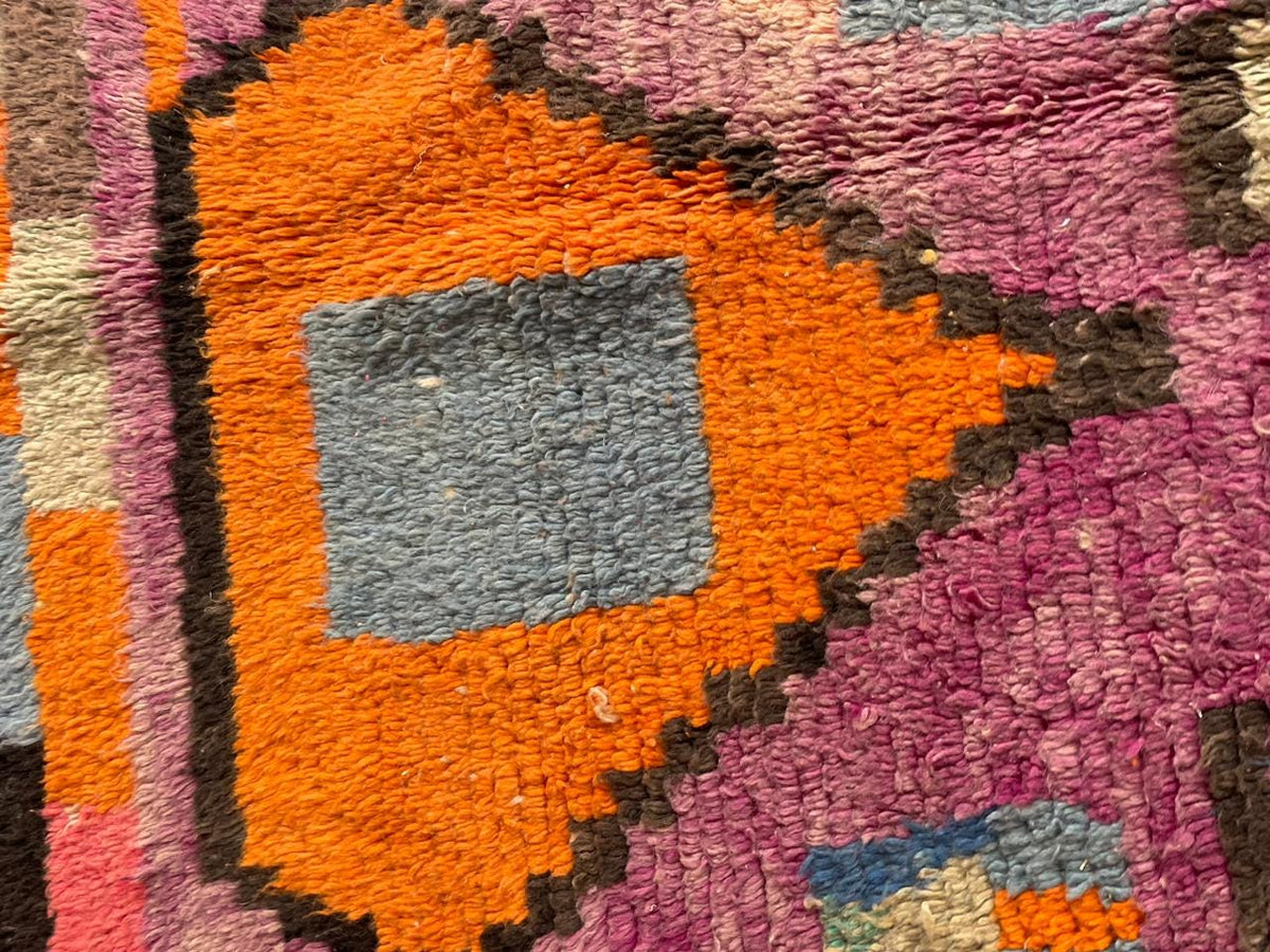 Close-up detail of varied patterns on a vintage Moroccan rug in purple and orange.
