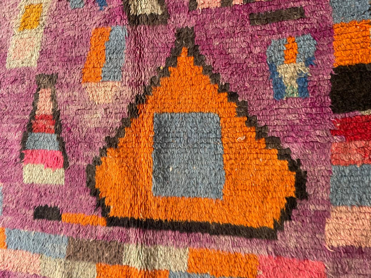 Close-up detail of geometric patterns on a vintage Moroccan rug featuring orange and purple.