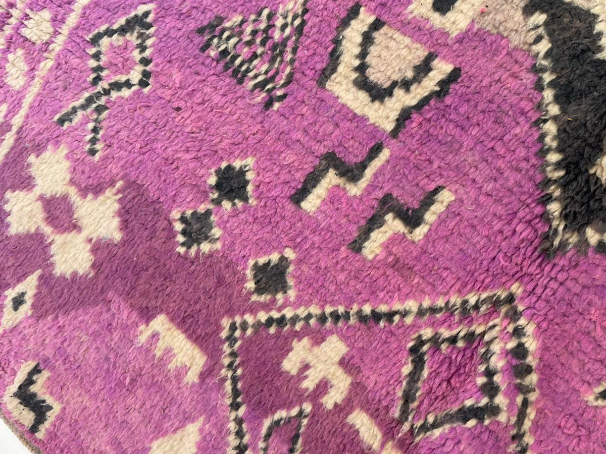 Close-up detail of a vintage Moroccan rug highlighting abstract motifs in purple and beige.