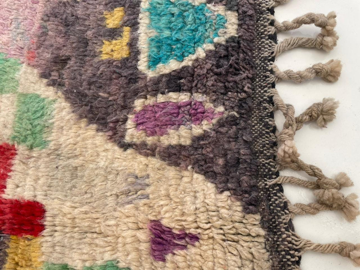 Close-up detail of a vintage Moroccan rug showcasing fringe edges and colorful motifs.