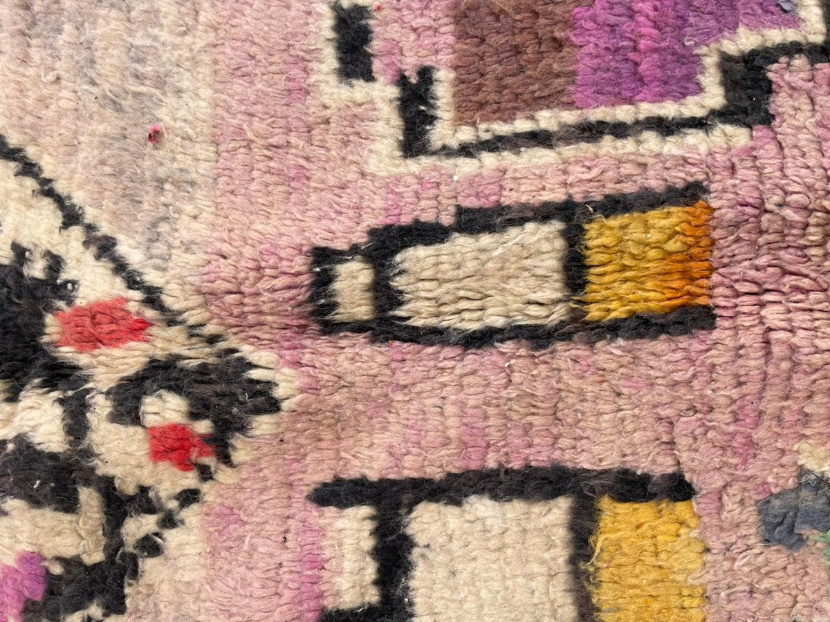 Close-up detail of a vintage Moroccan rug with abstract designs in purple, yellow, and black.
