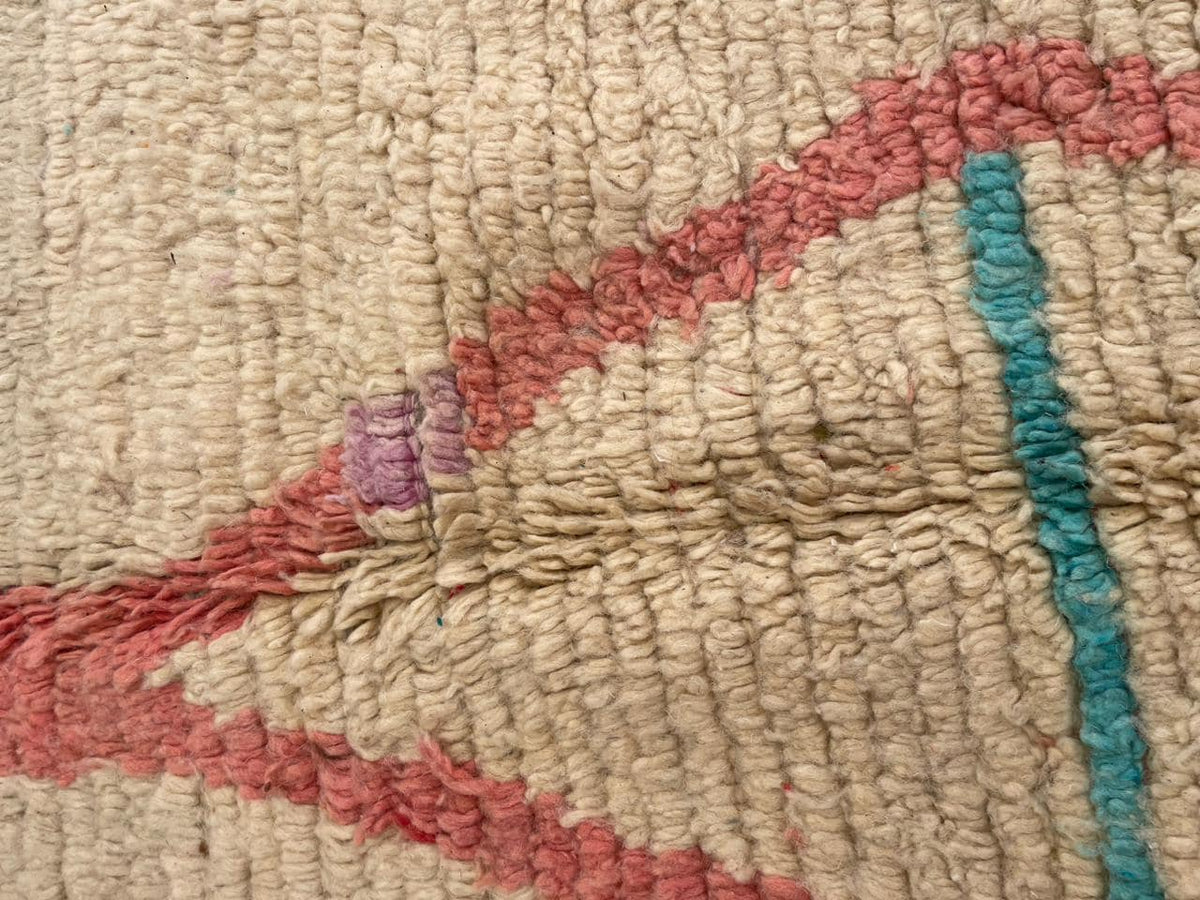 Close-up detail of a vintage Moroccan rug with tribal patterns in beige, red, blue, and purple.