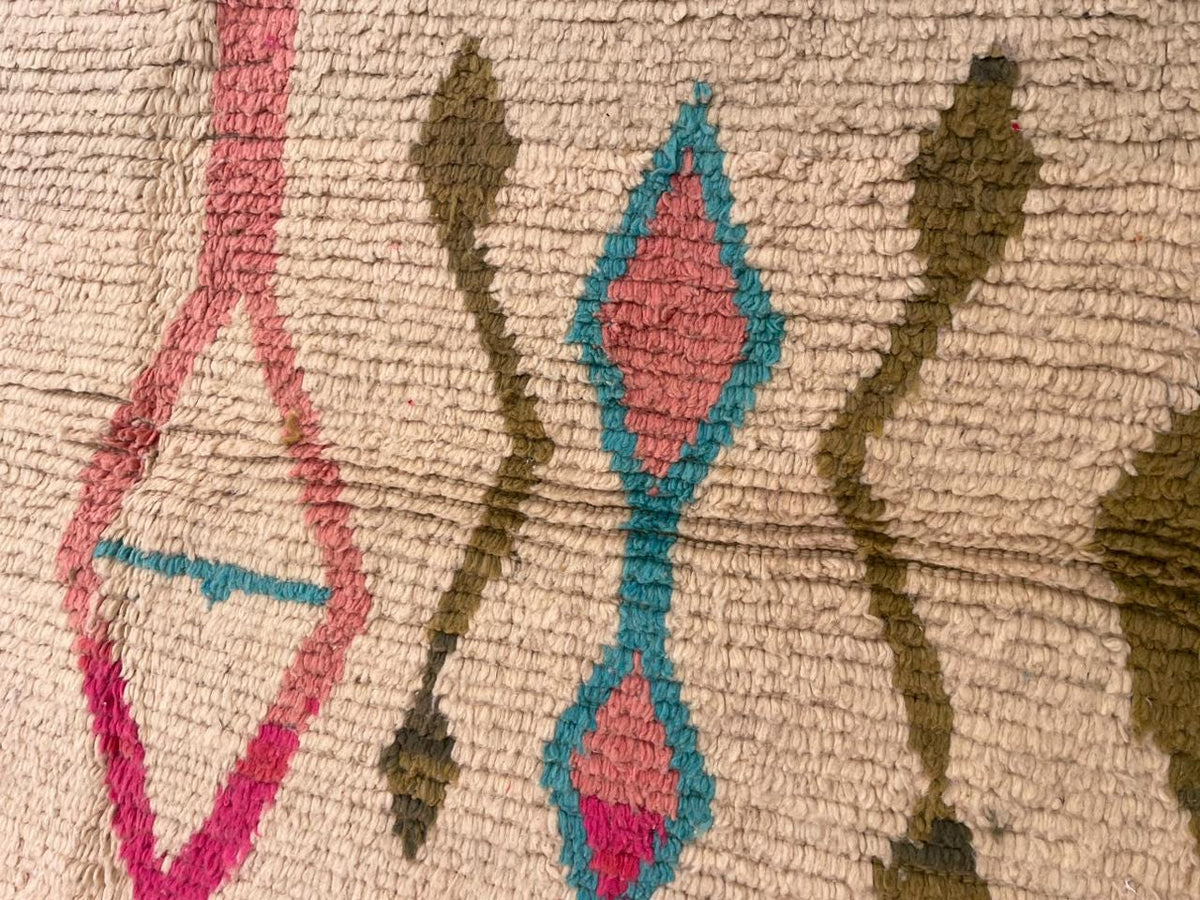 Close-up detail of a vintage Moroccan rug featuring tribal patterns in beige, red, blue, and green.