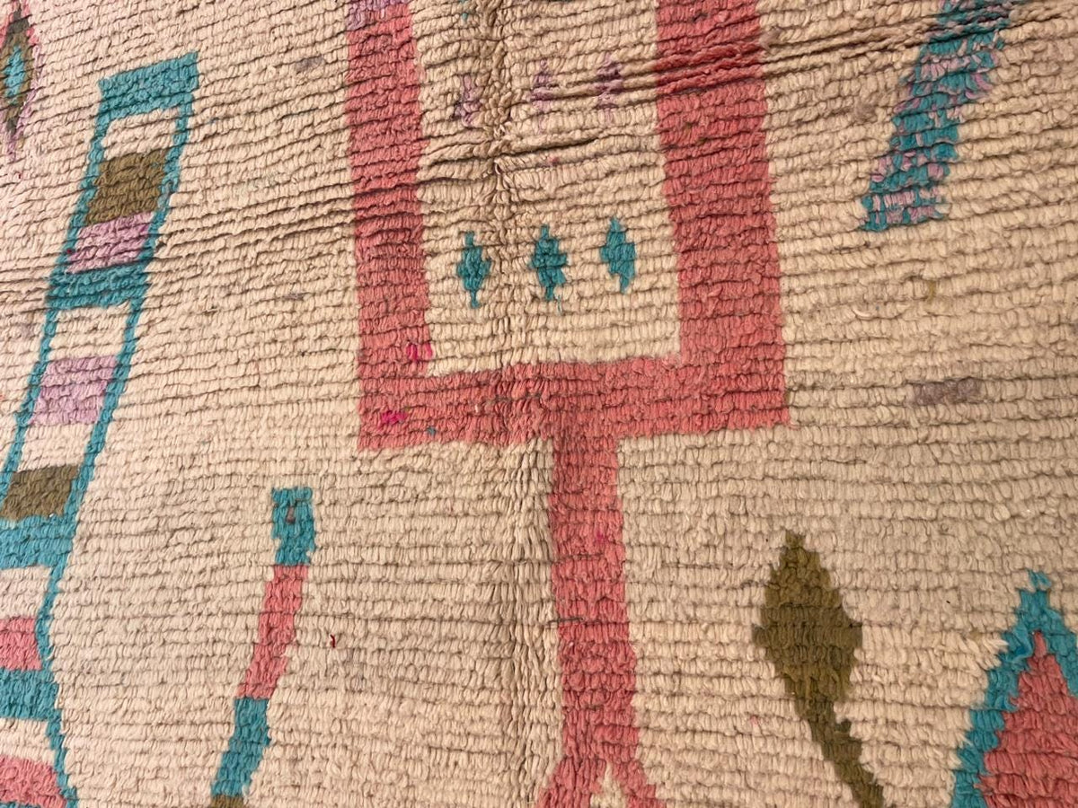 Close-up detail of a vintage Moroccan rug displaying tribal patterns in beige, red, blue, and green.