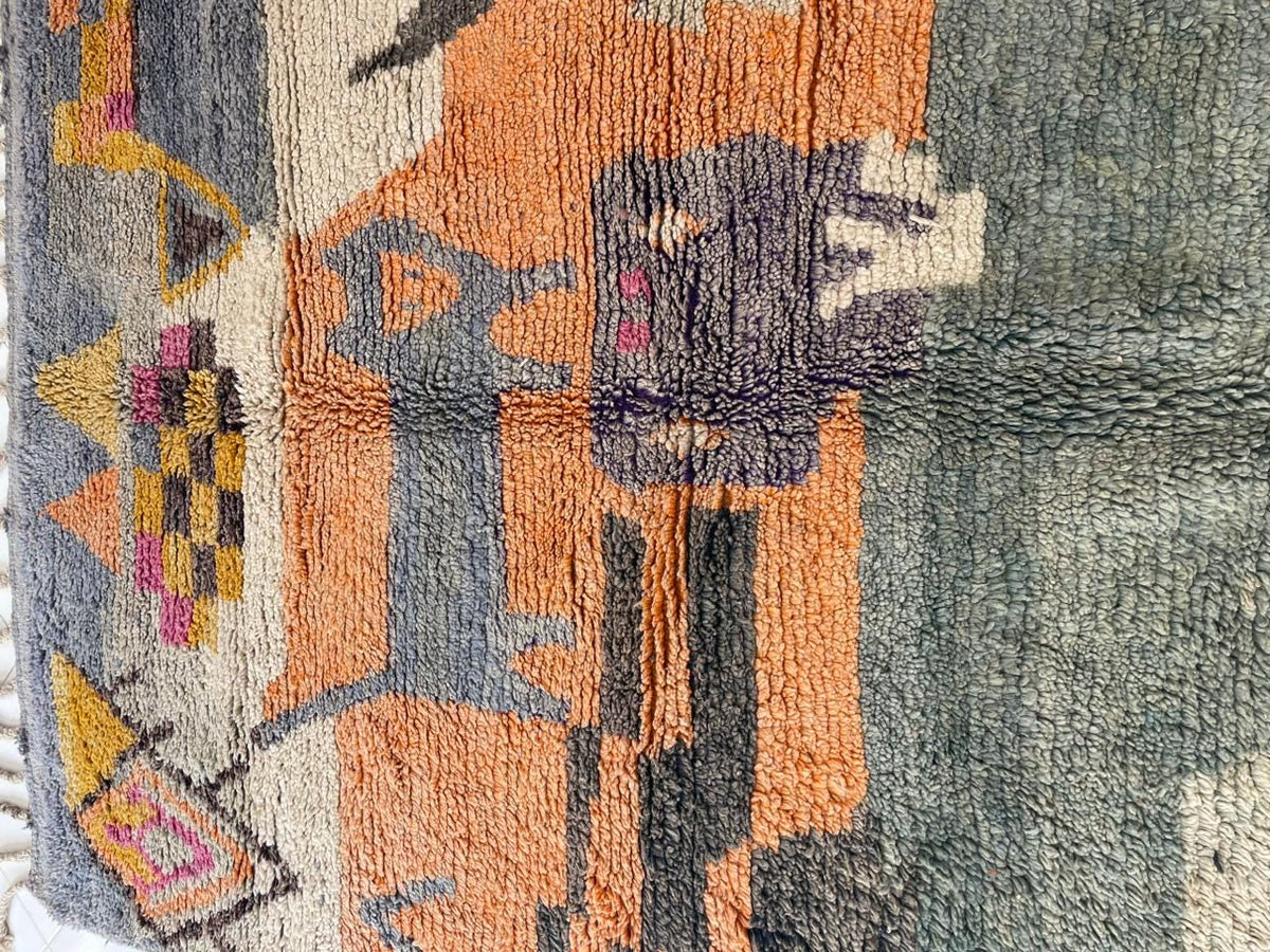 Close-up detail of a vintage Moroccan rug highlighting tribal patterns and fringe edges against a white backdrop.
