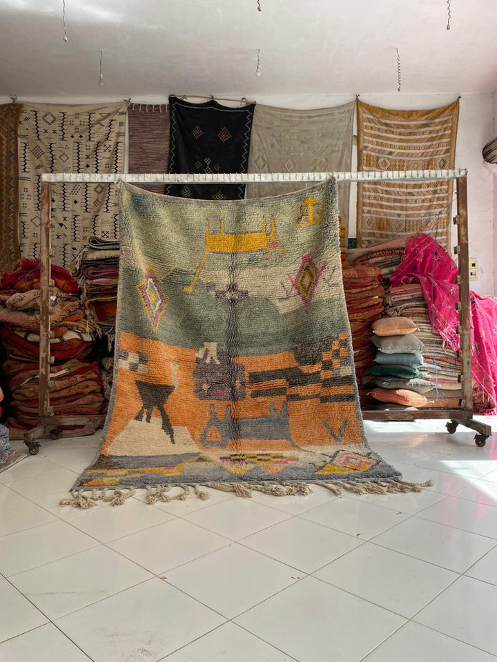 Lifestyle shot of a vintage Moroccan rug featuring tribal patterns in orange, blue, and green.