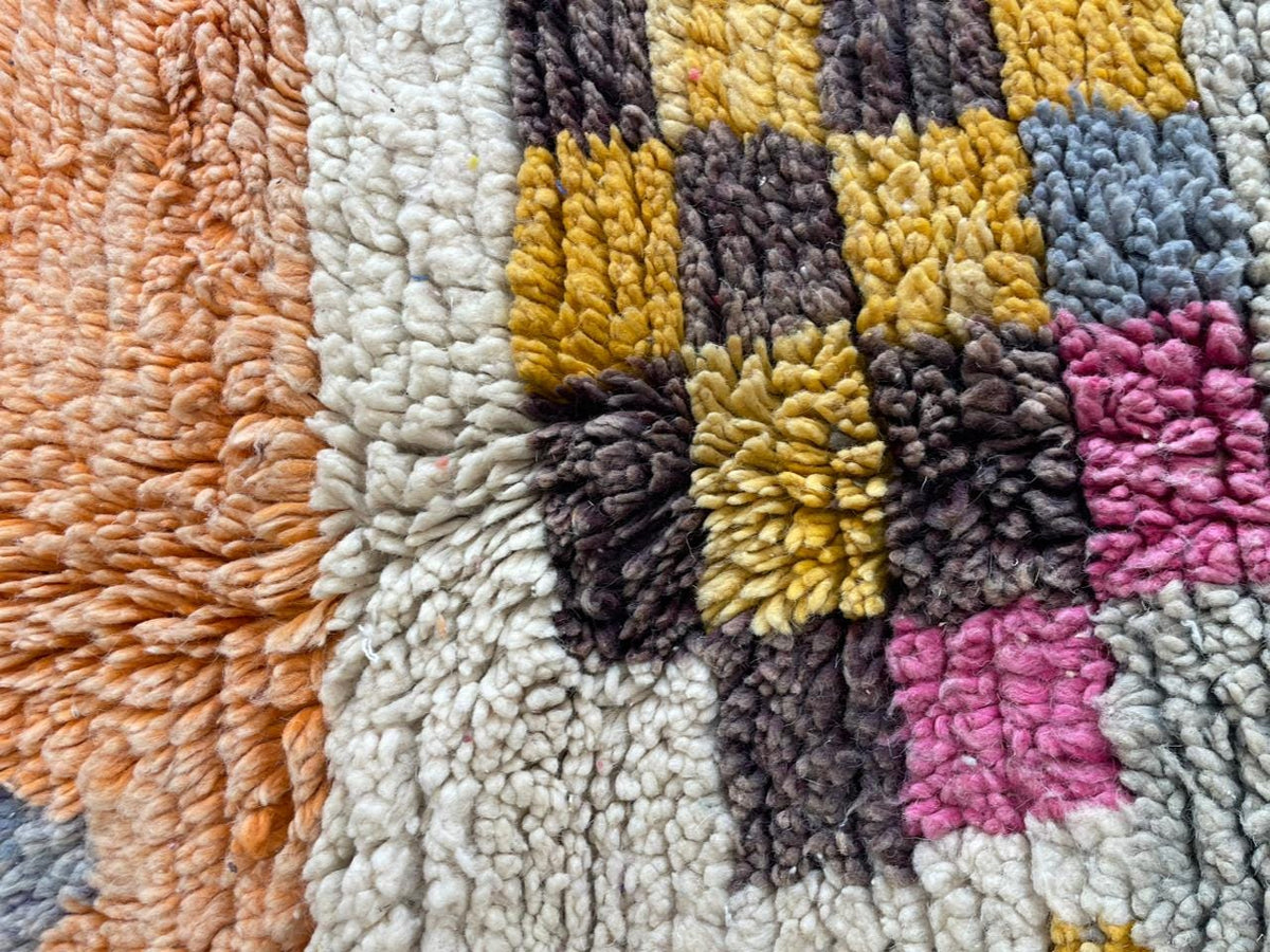 Close-up detail of a vintage Moroccan rug featuring tribal patterns in orange, yellow, purple, and white.