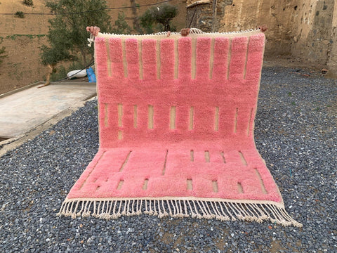 Lifestyle image of a pink Moroccan rug displaying geometric patterns and fringe edges.