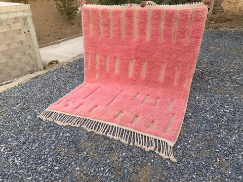 Other angle of a pink Moroccan rug with geometric designs and fringe edges.