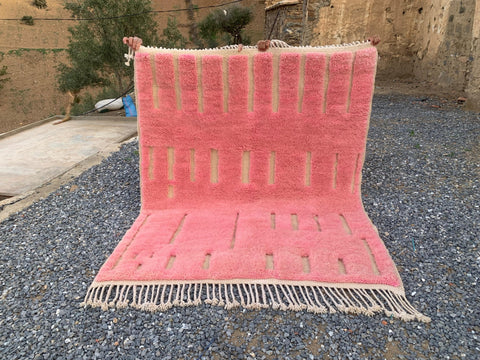 Lifestyle shot of a pink Moroccan rug featuring geometric patterns and fringe edges.
