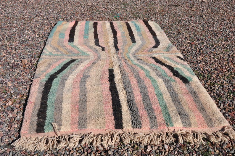 Lifestyle depiction of a pink striped Moroccan rug with fringe edges in a natural environment.