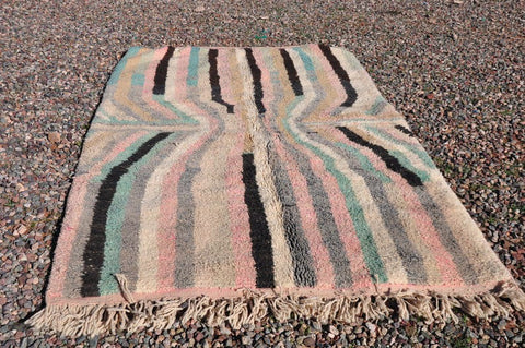 Lifestyle depiction of a pink striped Moroccan rug with fringe edges in a natural environment.