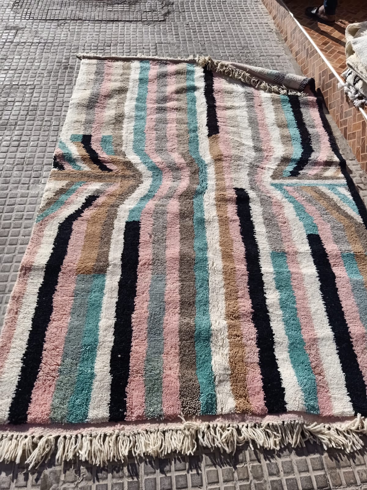 Lifestyle angle of a pink striped Moroccan rug showcasing fringe edges in a different background.