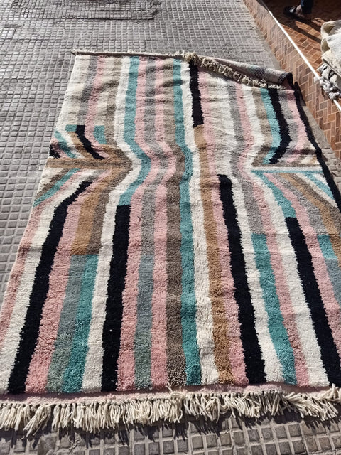 Lifestyle angle of a pink striped Moroccan rug showcasing fringe edges in a different background.