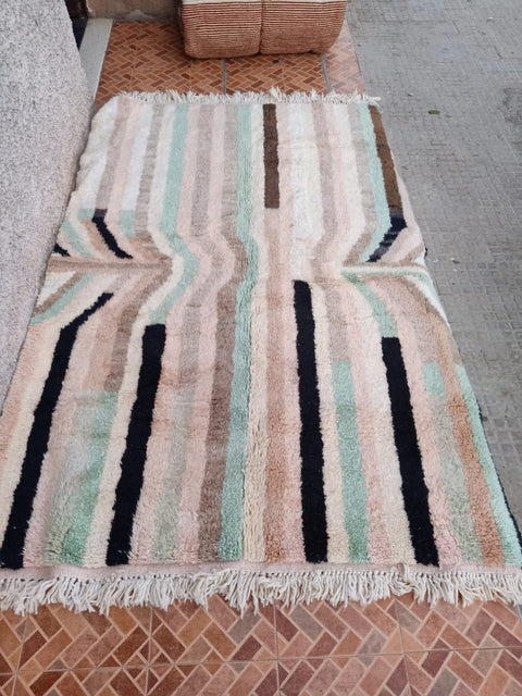 Lifestyle view of a pink striped Moroccan rug featuring fringe edges against a natural background.