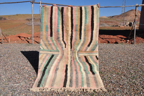 Lifestyle shot of a pink striped Moroccan rug with fringe edges in a natural setting.