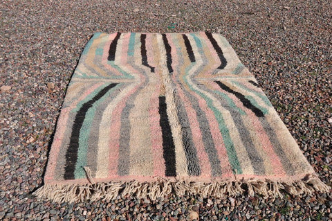 Close-up view of a pink striped Moroccan rug featuring fringe edges in a natural background.