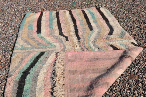 Close-up of a pink striped Moroccan rug with fringe edges in a natural setting, highlighting the striped pattern.