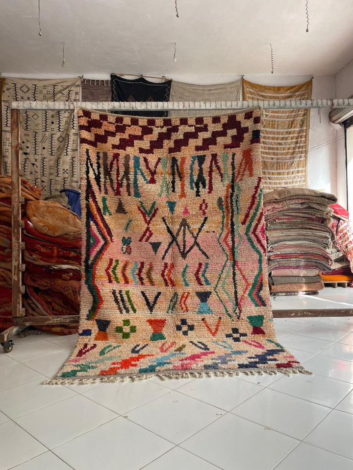 Lifestyle shot of a beige and red Moroccan rug with geometric patterns on a natural background.