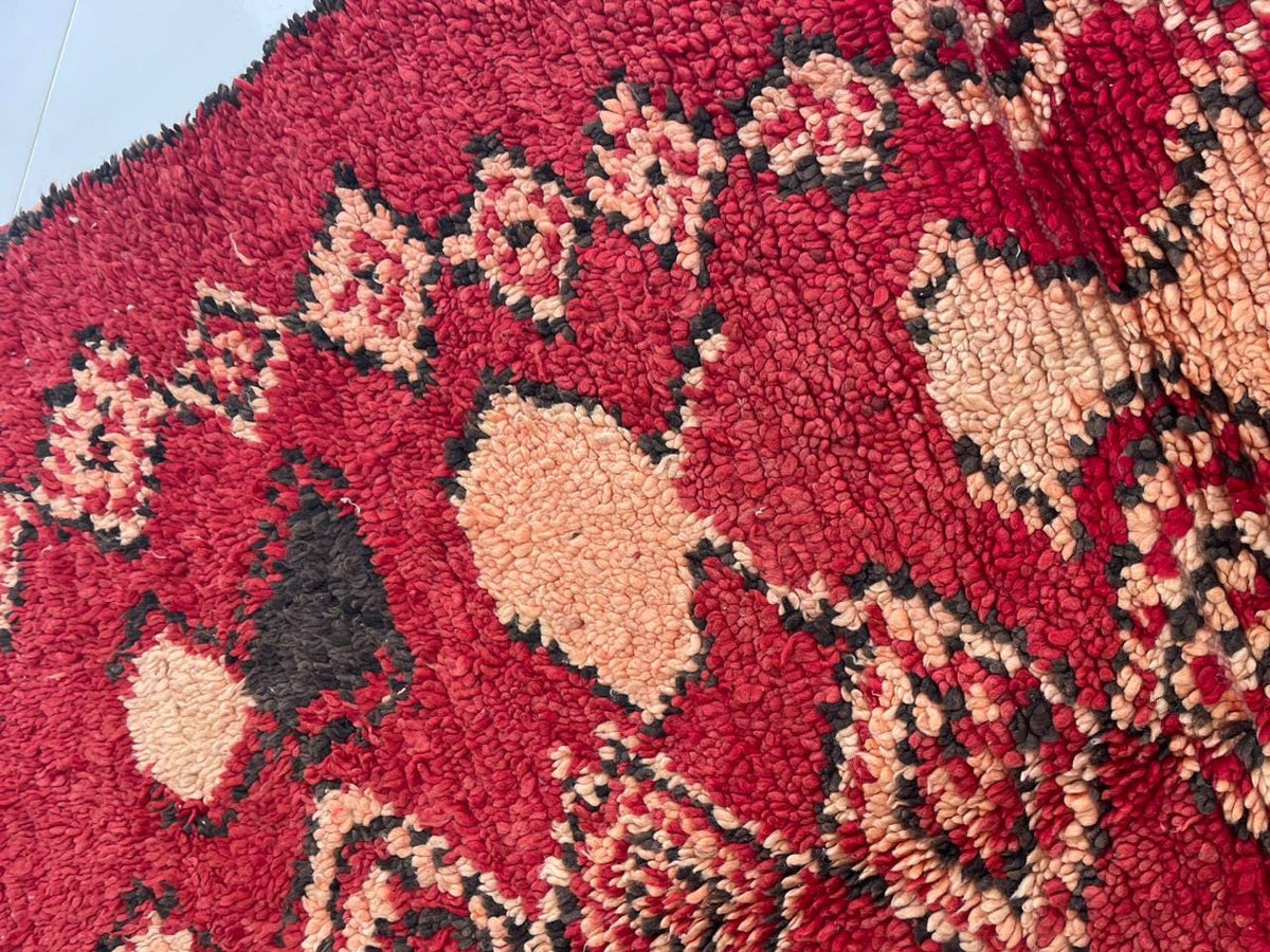 Close-up of geometric patterns on a red vintage Moroccan rug set against a white background.