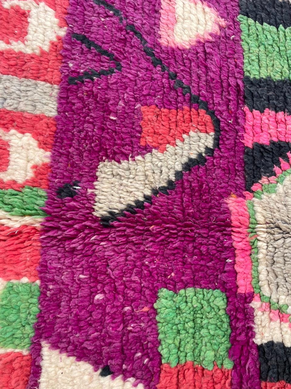 Close-up detail of a vintage Moroccan rug with tribal patterns in red, pink, and white.
