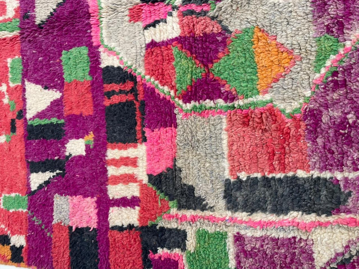 Detail shot of the tribal pattern on a red vintage Moroccan rug with colors of purple and pink.