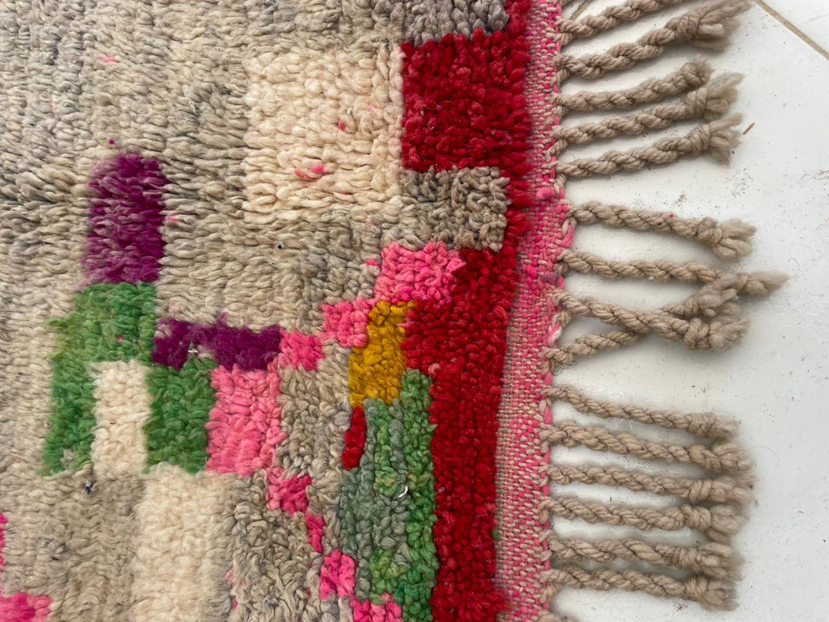 Close-up detail of a vintage Moroccan rug with tribal patterns and fringe edges in red and beige.