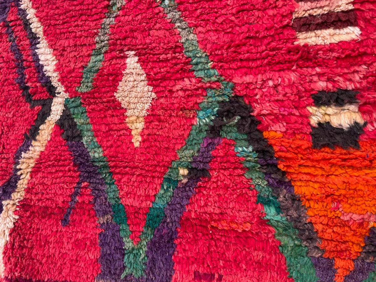 Close-up detail of a red vintage Moroccan rug displaying diamond shapes and tribal patterns.