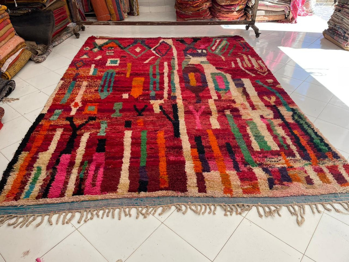 Close-up detail of a red vintage Moroccan rug featuring fringe edges and colorful patterns.