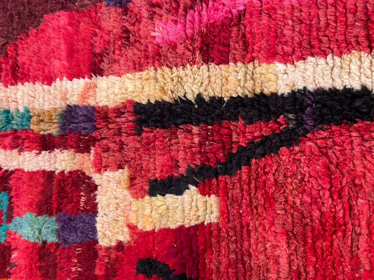 Close-up detail of a red vintage Moroccan rug featuring tribal patterns with a mix of colors.