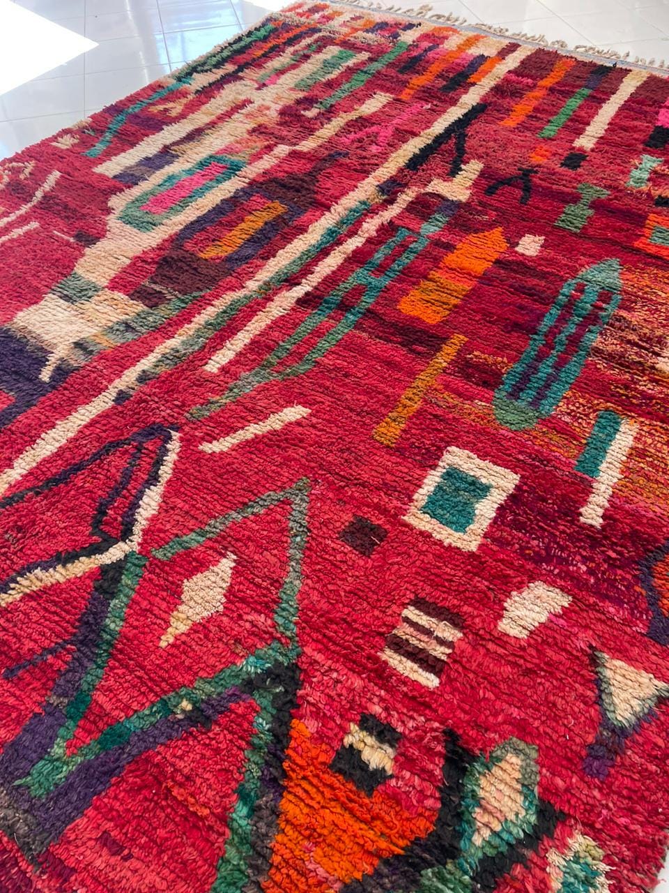 Close-up detail of a red vintage Moroccan rug with abstract designs against a natural background.
