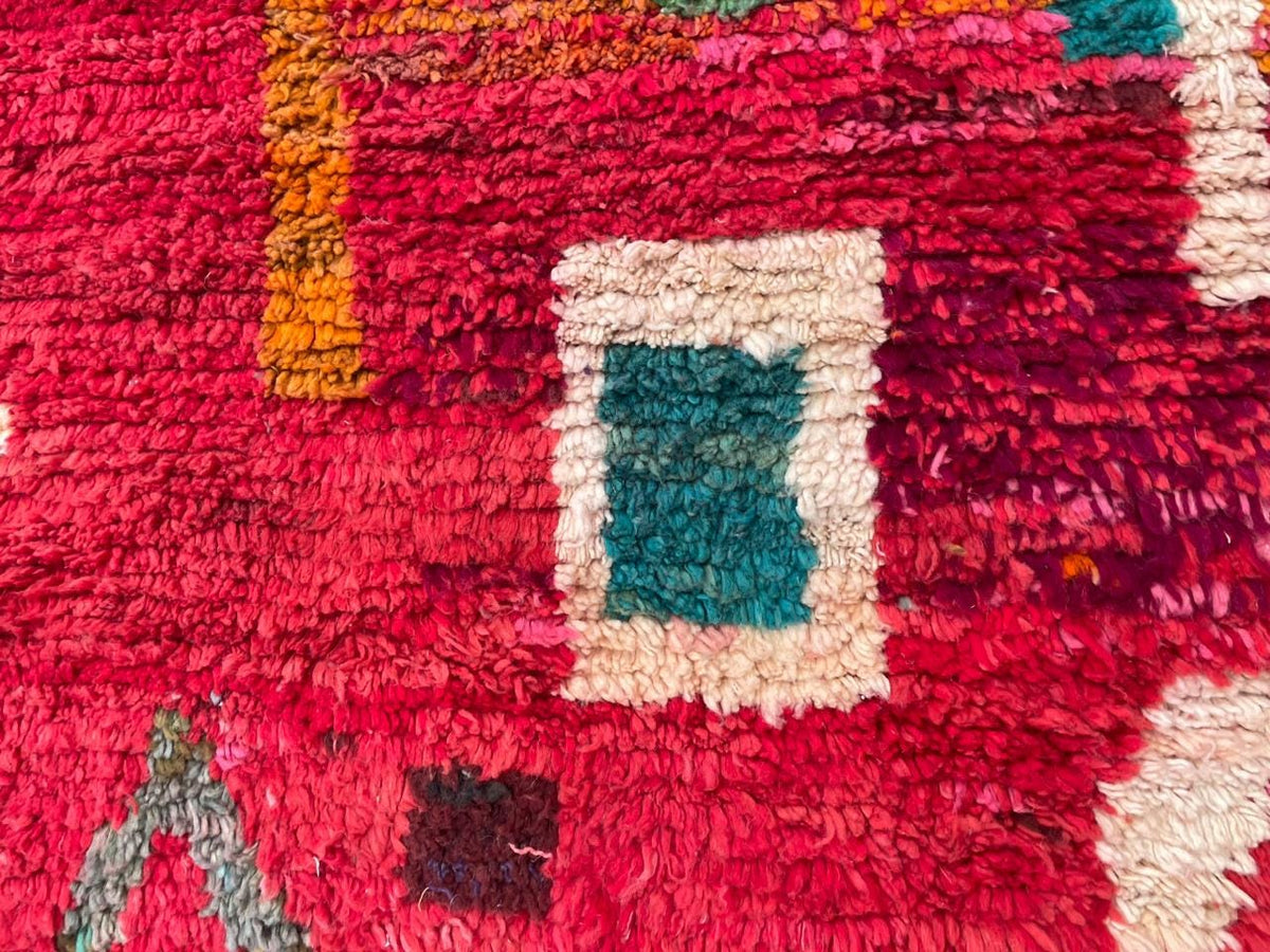 Detail shot of a red vintage Moroccan rug showing tribal patterns and texture in various colors.