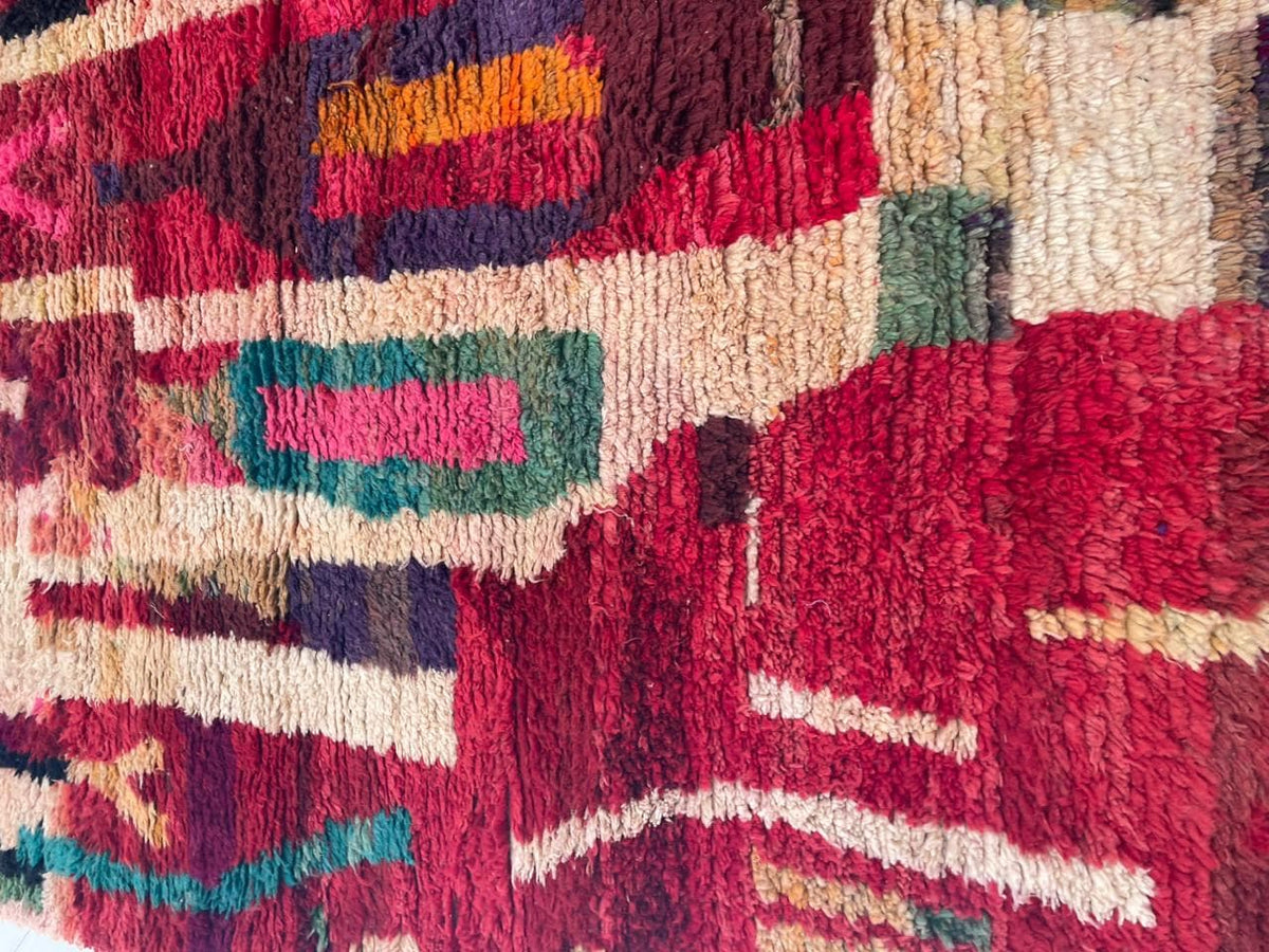 Detail shot of a red vintage Moroccan rug featuring tribal patterns in a mix of colors.