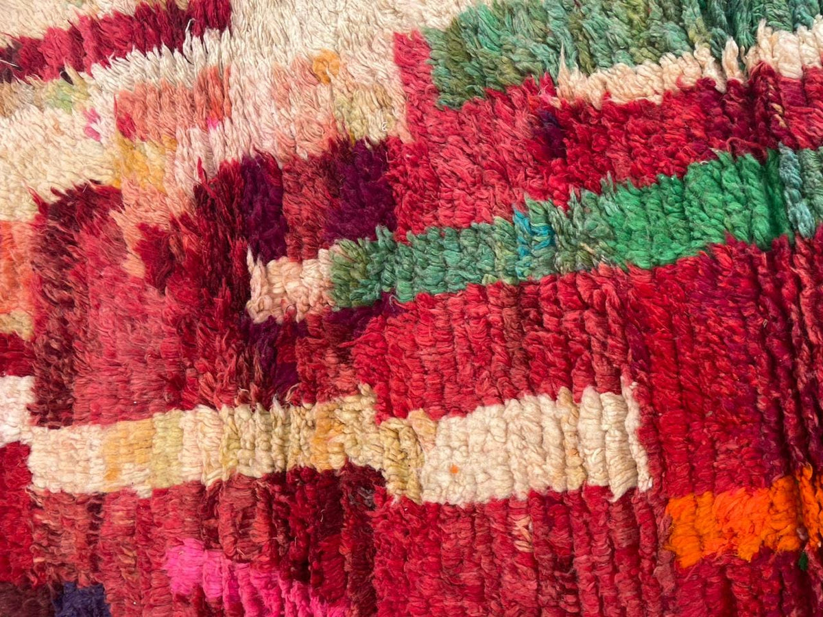 Detail shot of a red vintage Moroccan rug displaying tribal patterns and wool texture.