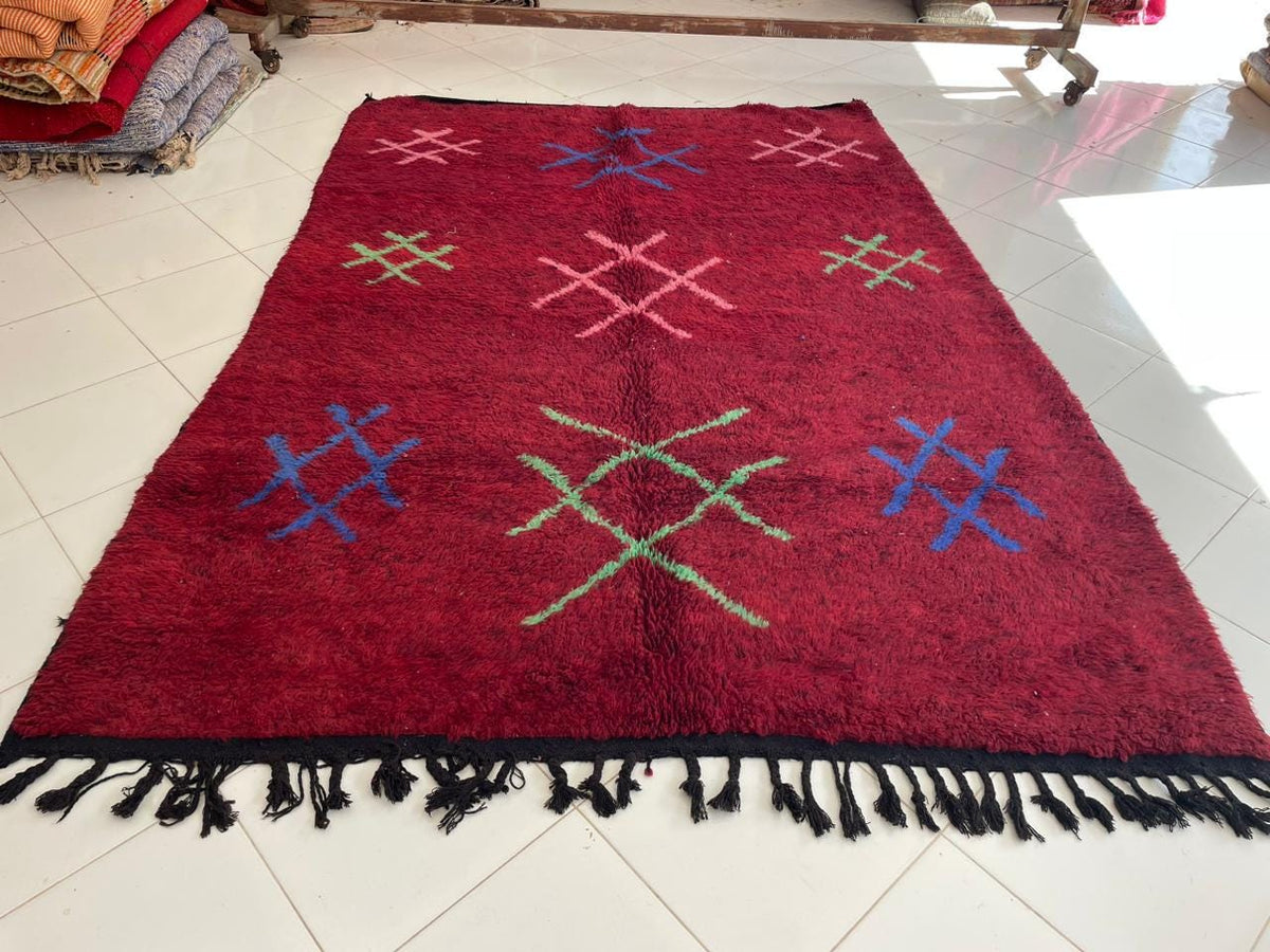 Top view of a red vintage Moroccan rug showcasing tribal designs with blue and green accents.