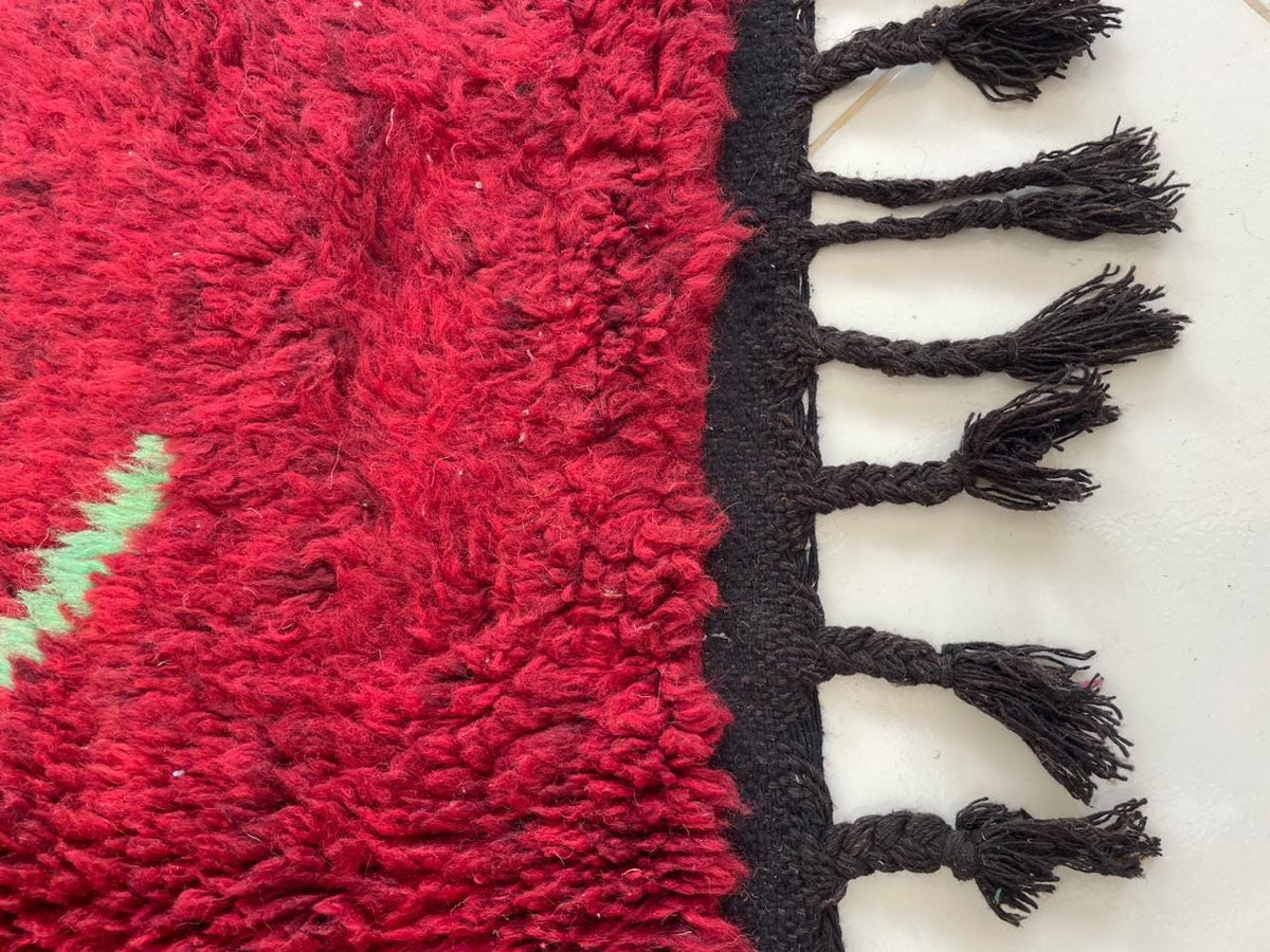 Detail shot of a red vintage Moroccan rug showcasing fringe edges and a textured surface.