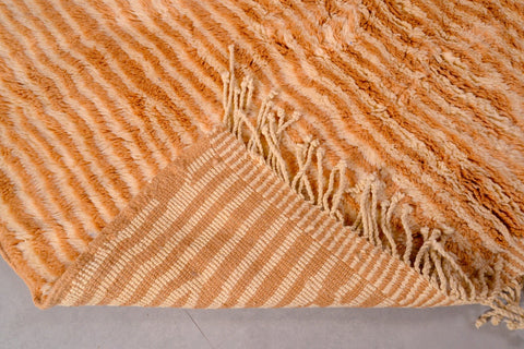 Detail close-up of an orange and beige Moroccan Mrirt rug with a striped pattern and fringed edges.