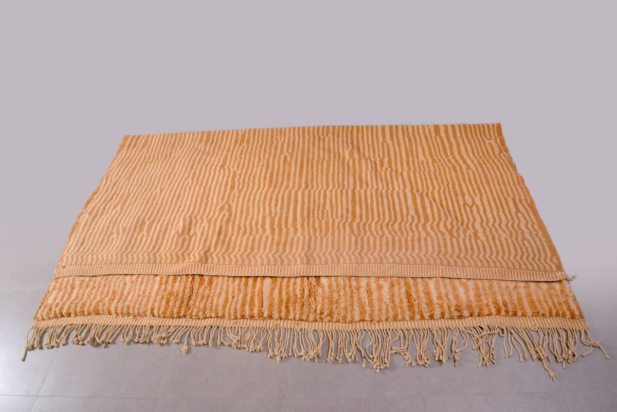 Detail close-up of a large orange and beige Moroccan Mrirt rug with fringe edges.