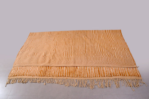 Detail close-up of a large orange and beige Moroccan Mrirt rug with fringe edges.