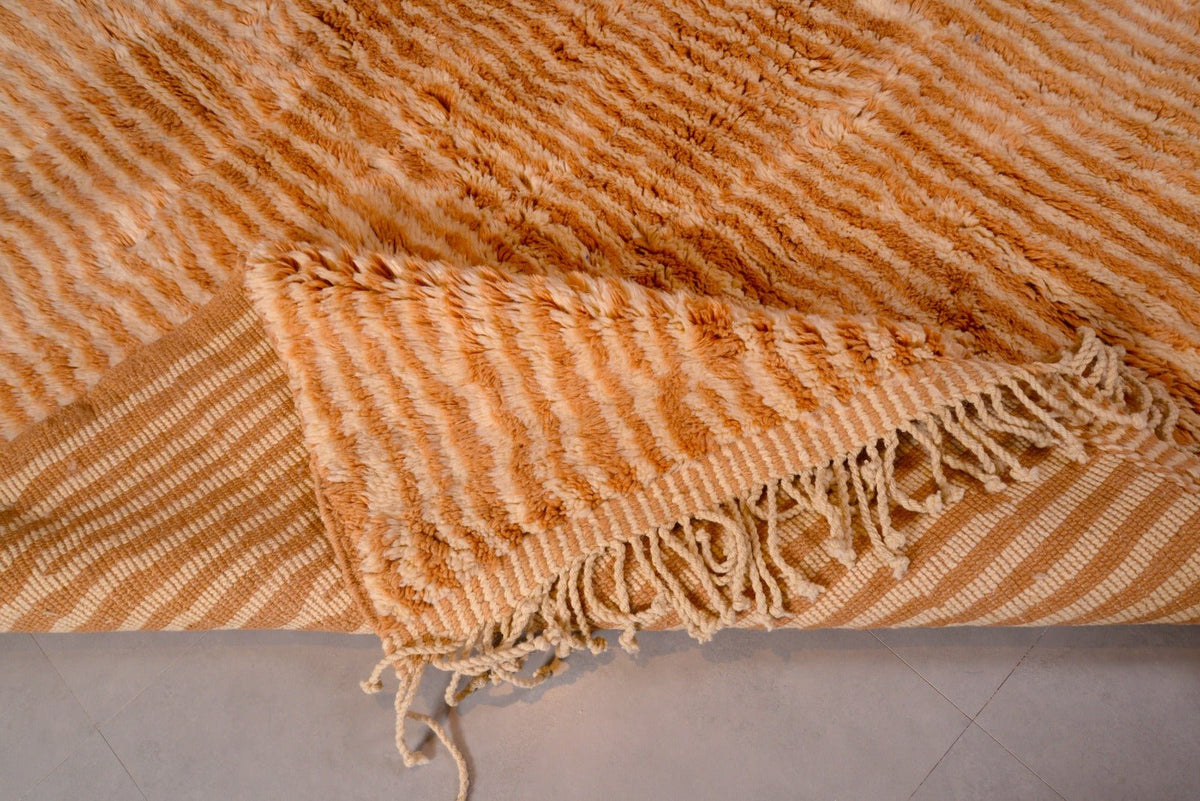 Detail close-up of an orange and beige Moroccan Mrirt rug featuring a striped pattern and fringe edges.