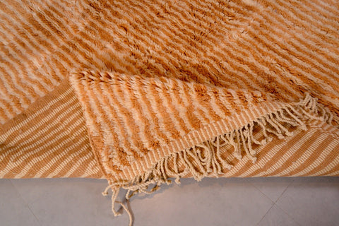 Detail close-up of an orange and beige Moroccan Mrirt rug featuring a striped pattern and fringe edges.