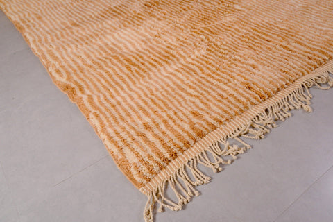 Detail close-up of an orange and beige Moroccan Mrirt rug with a soft texture and fringe edges.