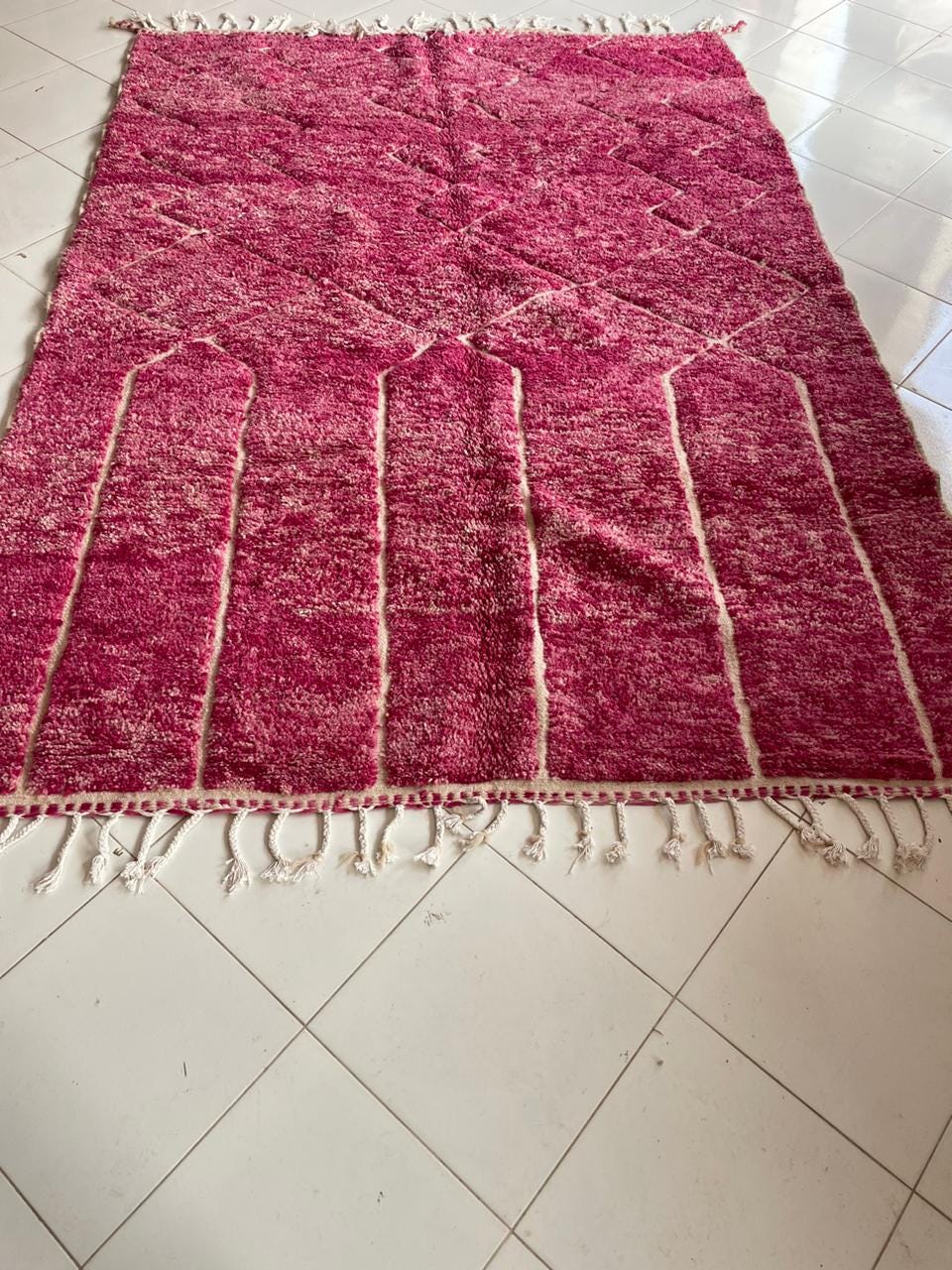 Lifestyle shot of a pink Moroccan rug with geometric patterns and fringe edges.